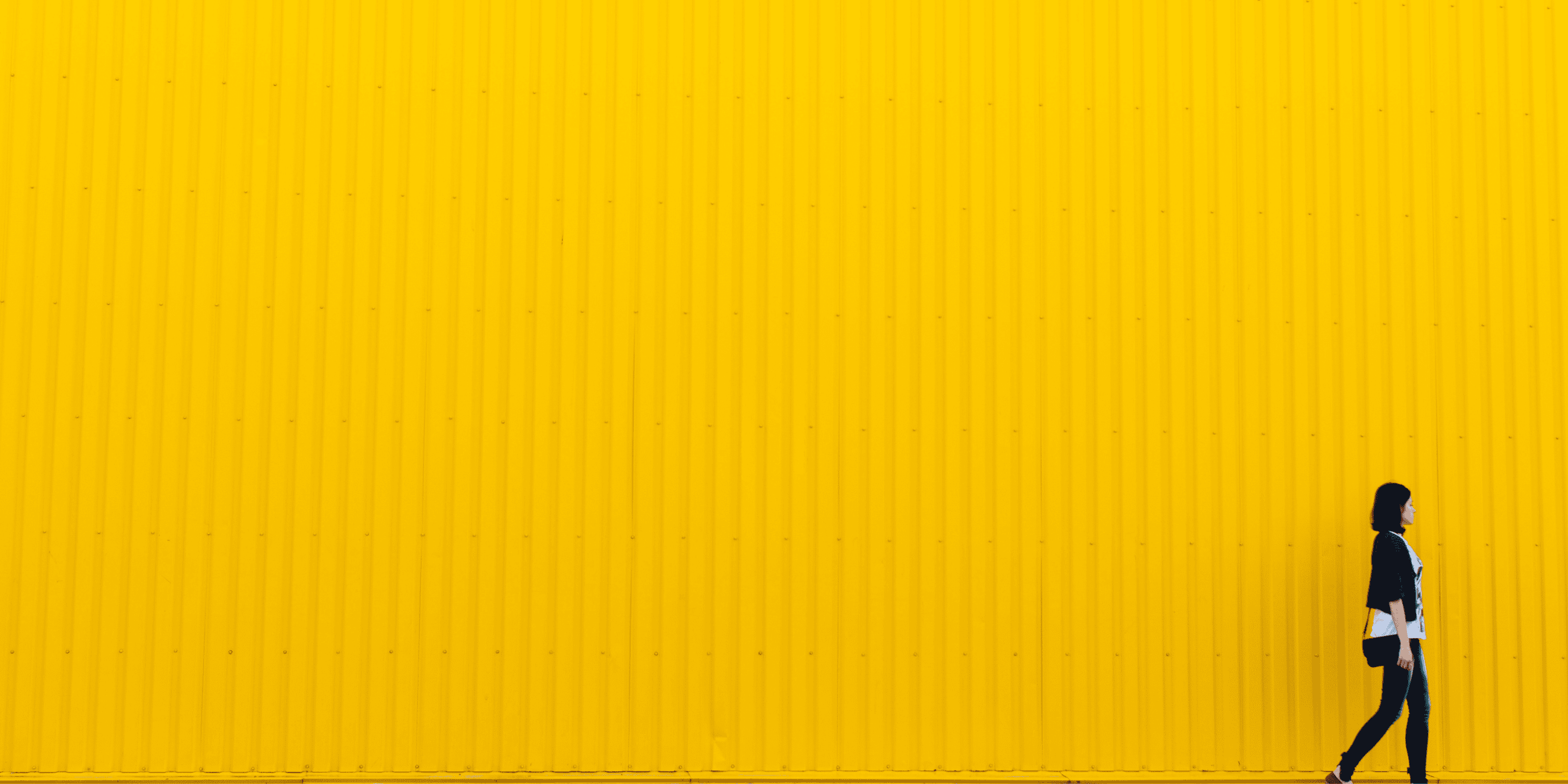 Figura femminile cammina lungo un alto muro giallo.